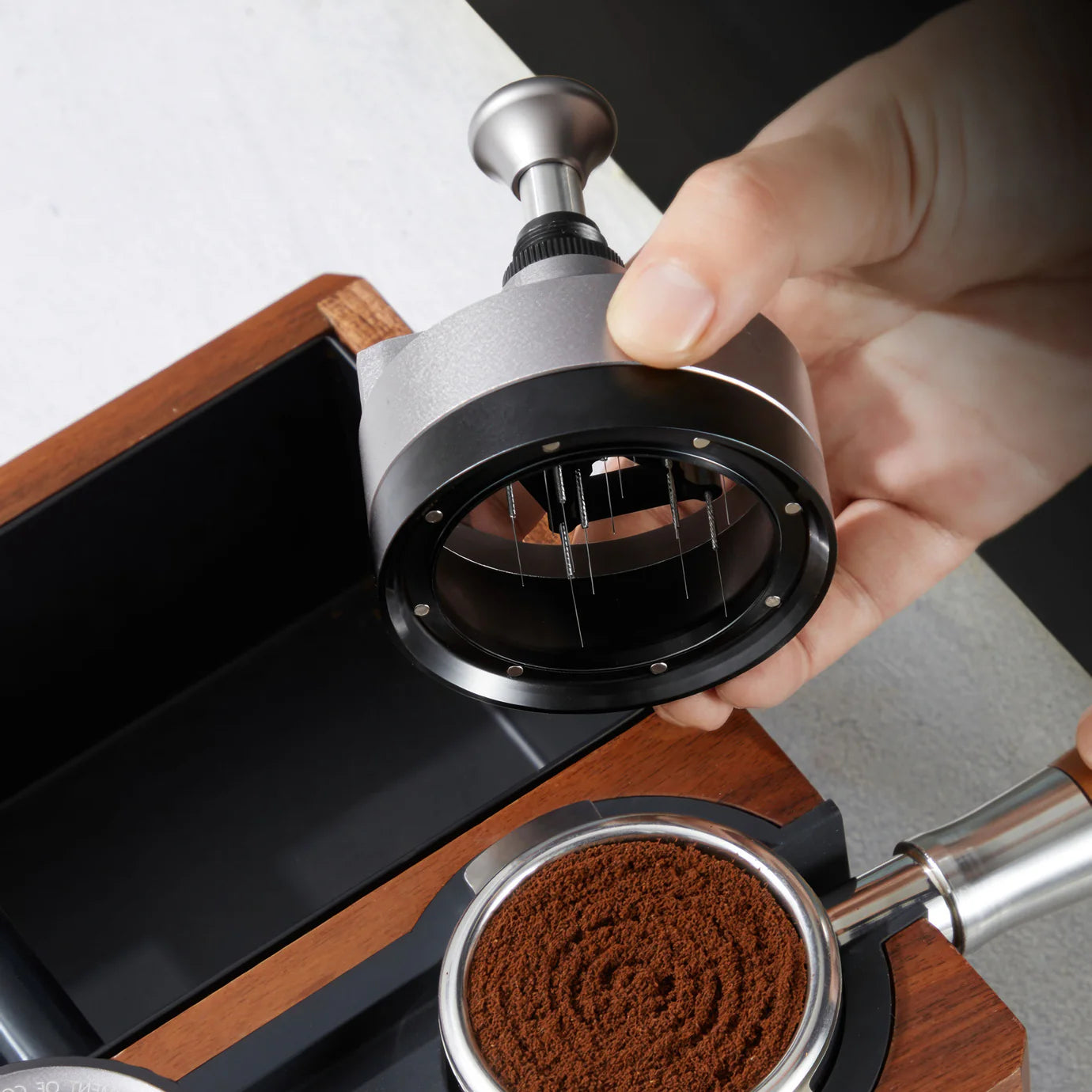 ZeroHero 58mm Sword Needle Distributor held above a portafilter filled with ground coffee.